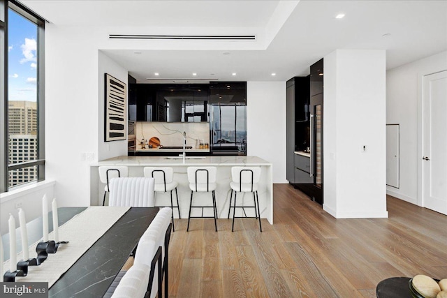 kitchen with kitchen peninsula, stainless steel fridge with ice dispenser, backsplash, light hardwood / wood-style floors, and a breakfast bar