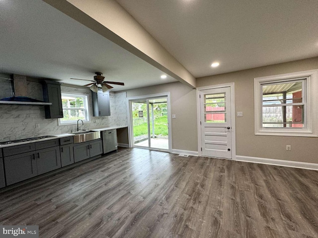 kitchen with wall chimney exhaust hood, sink, tasteful backsplash, gas stovetop, and hardwood / wood-style flooring