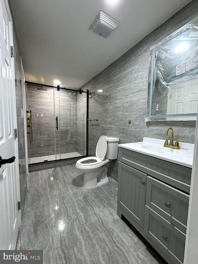 bathroom with tile flooring, tile walls, toilet, a shower with shower door, and vanity