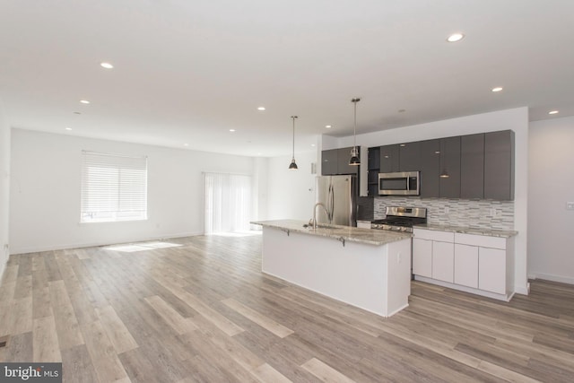 kitchen with stainless steel appliances, tasteful backsplash, an island with sink, sink, and light wood-type flooring