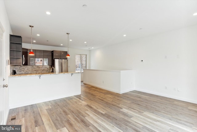 kitchen featuring pendant lighting, light wood-type flooring, dark brown cabinets, tasteful backsplash, and stainless steel fridge