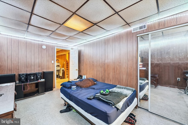 carpeted bedroom with a closet, a drop ceiling, and wooden walls