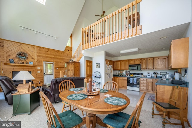 carpeted dining area with high vaulted ceiling, wood walls, ceiling fan, and rail lighting