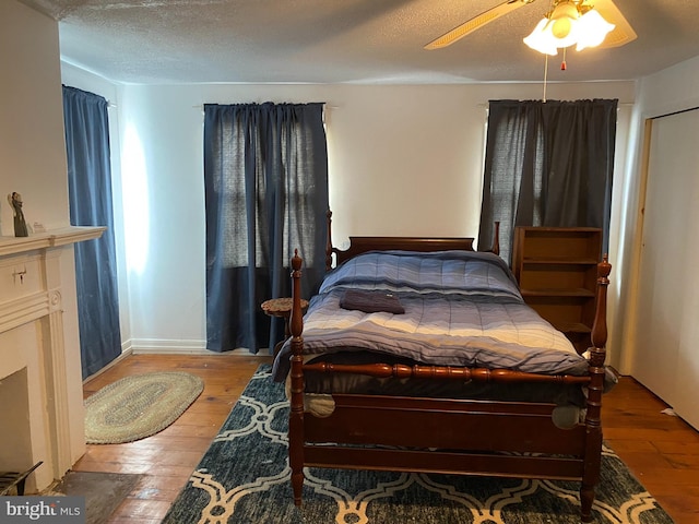 bedroom with a textured ceiling, ceiling fan, hardwood / wood-style floors, and a fireplace