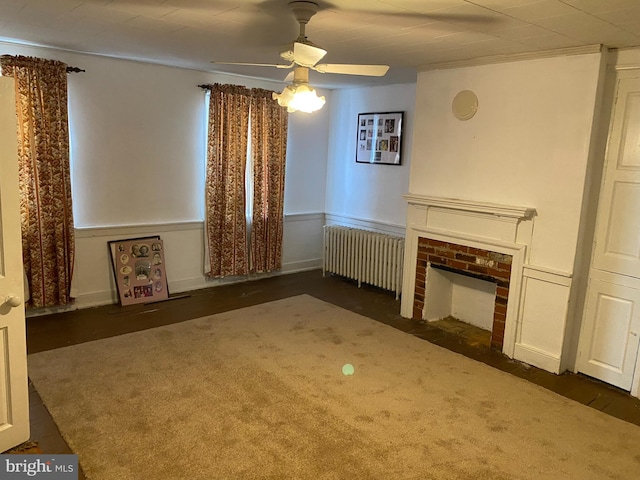 unfurnished living room with radiator, a brick fireplace, and ceiling fan