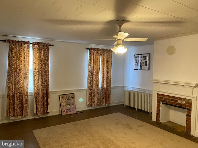 unfurnished living room featuring radiator, a brick fireplace, and ceiling fan