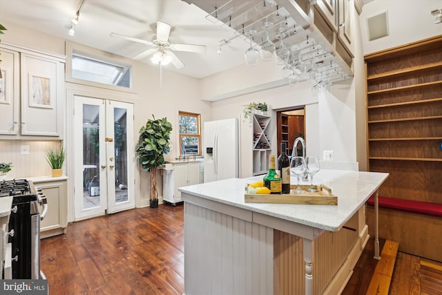 kitchen featuring french doors, black range, a kitchen breakfast bar, light stone countertops, and white fridge with ice dispenser