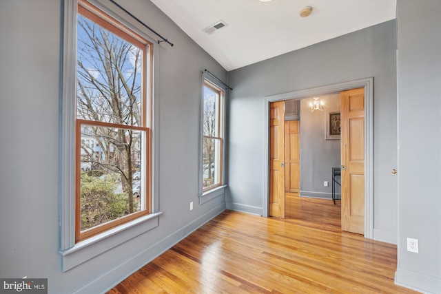 empty room with a notable chandelier, light wood-type flooring, and a wealth of natural light