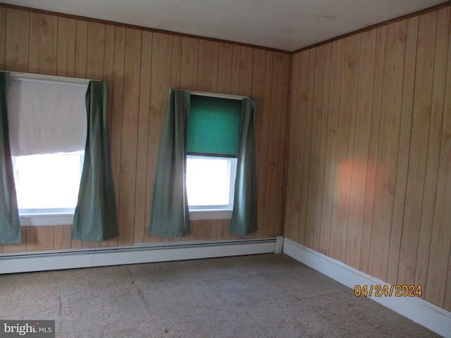 empty room with carpet, a baseboard heating unit, and wood walls