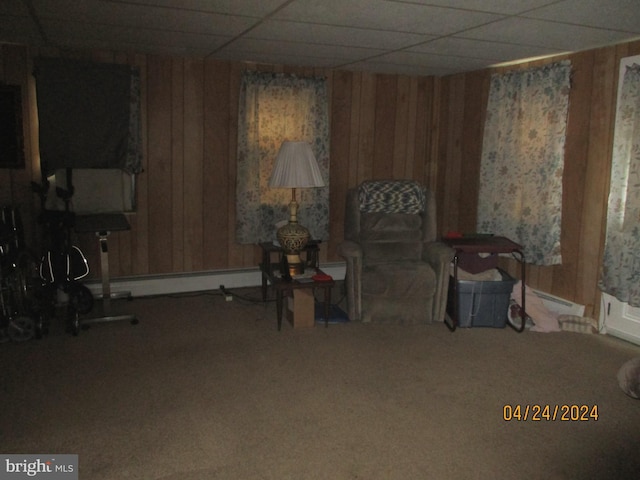 living area featuring carpet, a paneled ceiling, baseboard heating, and wooden walls