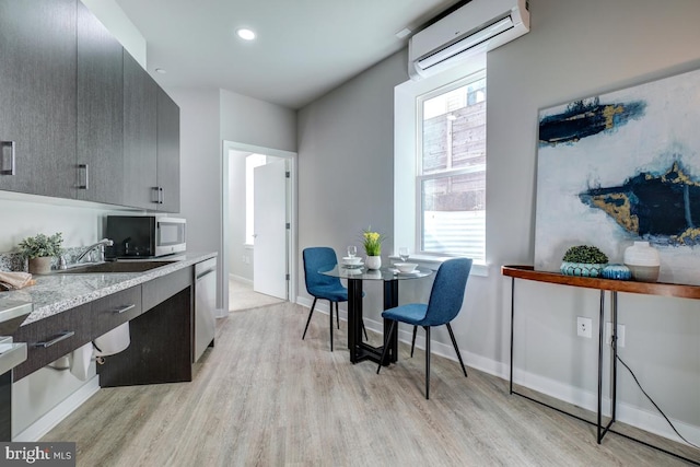 kitchen with light wood-type flooring, stainless steel appliances, light stone counters, an AC wall unit, and sink