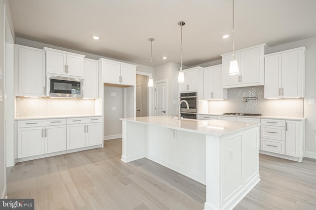 kitchen featuring white cabinets, tasteful backsplash, decorative light fixtures, stainless steel appliances, and a center island with sink