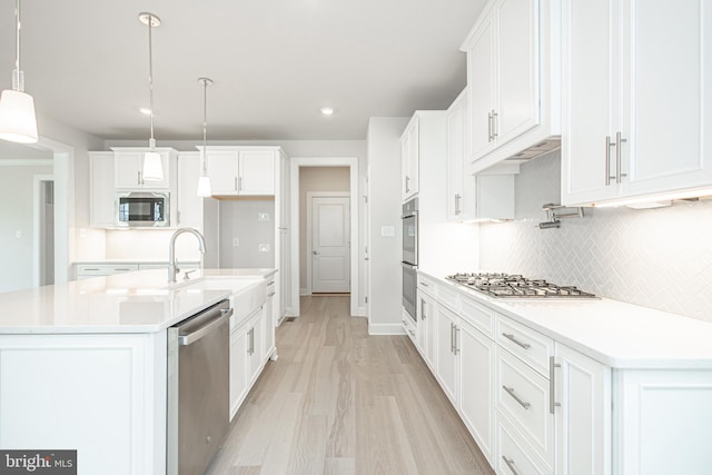 kitchen featuring backsplash, hanging light fixtures, stainless steel appliances, light hardwood / wood-style floors, and white cabinets