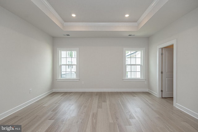 empty room featuring a healthy amount of sunlight, a raised ceiling, light wood-type flooring, and ornamental molding