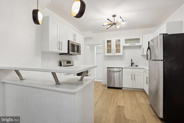 kitchen with appliances with stainless steel finishes, sink, white cabinetry, hanging light fixtures, and light hardwood / wood-style flooring