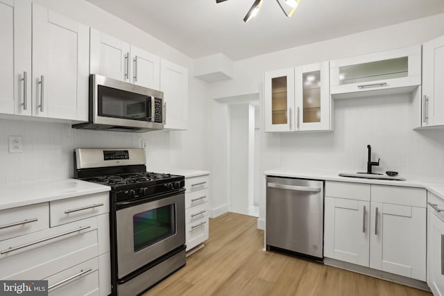 kitchen featuring light hardwood / wood-style flooring, white cabinetry, stainless steel appliances, sink, and tasteful backsplash