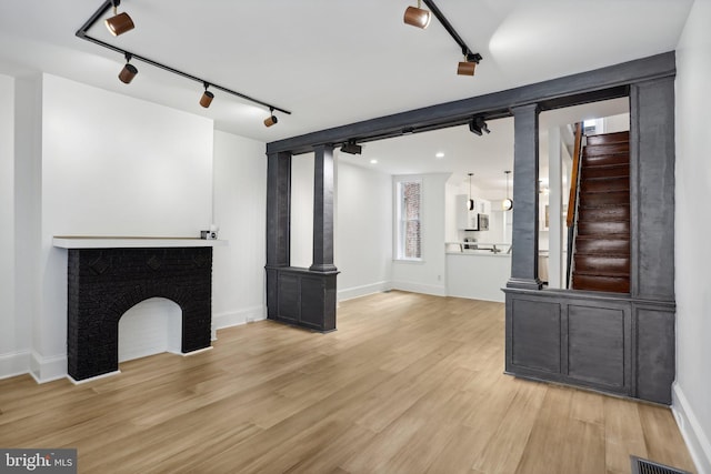 unfurnished living room with light hardwood / wood-style floors, rail lighting, and ornate columns