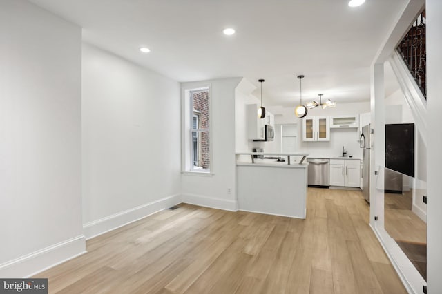 kitchen featuring decorative light fixtures, white cabinets, light wood-type flooring, appliances with stainless steel finishes, and sink