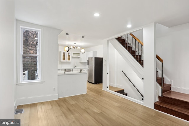 kitchen featuring stainless steel fridge, white cabinets, pendant lighting, light wood-type flooring, and a chandelier