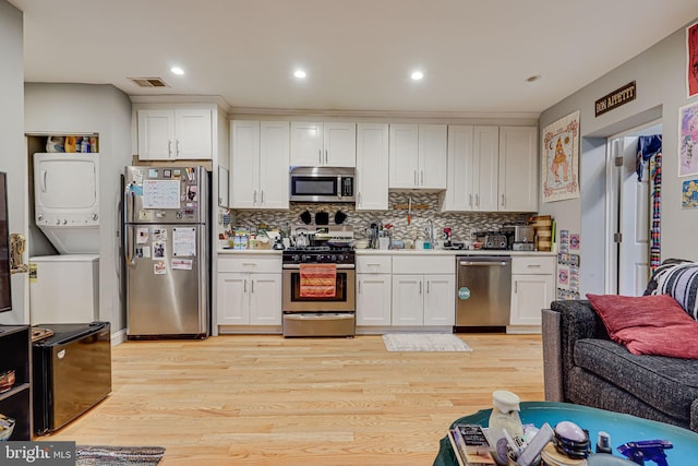 kitchen featuring stacked washer / dryer, stainless steel appliances, light hardwood / wood-style floors, and white cabinetry