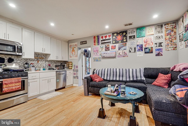 kitchen featuring backsplash, appliances with stainless steel finishes, white cabinetry, and light wood-type flooring