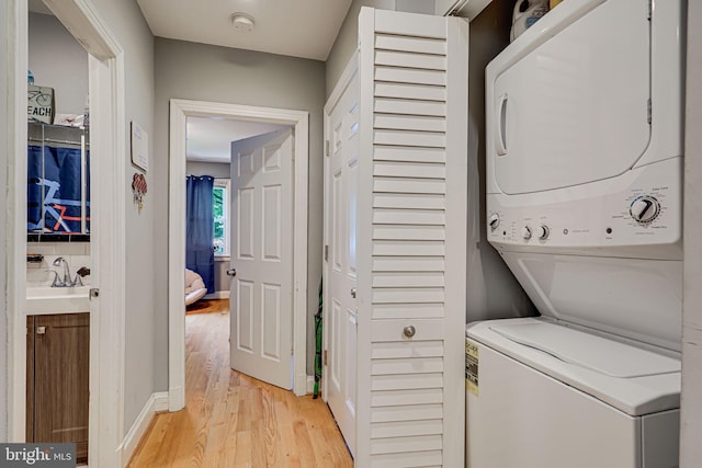 laundry area featuring stacked washer and clothes dryer, light hardwood / wood-style flooring, and sink