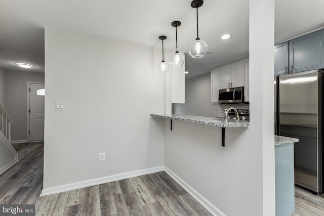 kitchen with light stone countertops, appliances with stainless steel finishes, hanging light fixtures, a breakfast bar area, and wood-type flooring