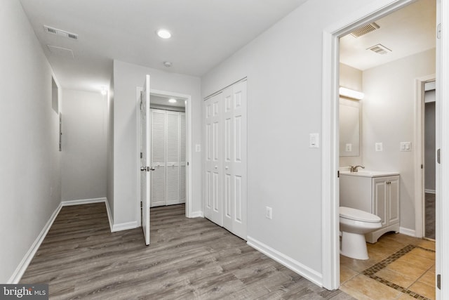 unfurnished bedroom featuring ensuite bath, light hardwood / wood-style flooring, and multiple closets