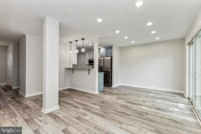 kitchen featuring stone countertops, light hardwood / wood-style floors, decorative light fixtures, stainless steel appliances, and kitchen peninsula