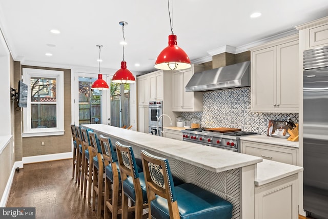 kitchen with dark hardwood / wood-style flooring, wall chimney exhaust hood, pendant lighting, high quality appliances, and cream cabinetry