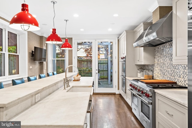 kitchen with pendant lighting, a kitchen breakfast bar, wall chimney range hood, sink, and appliances with stainless steel finishes