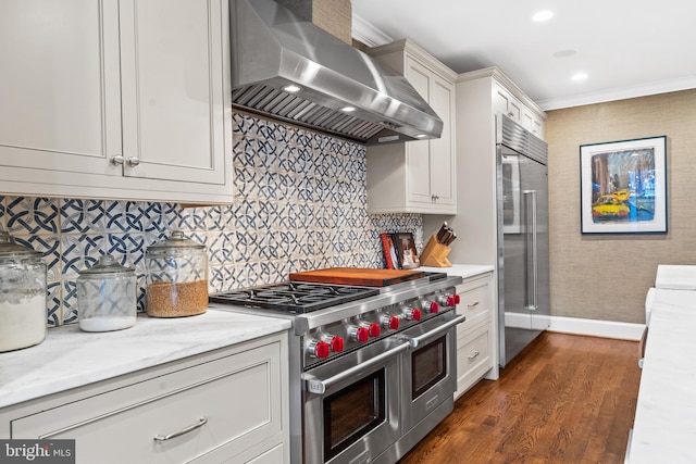 kitchen with wall chimney exhaust hood, premium appliances, crown molding, dark hardwood / wood-style floors, and white cabinetry