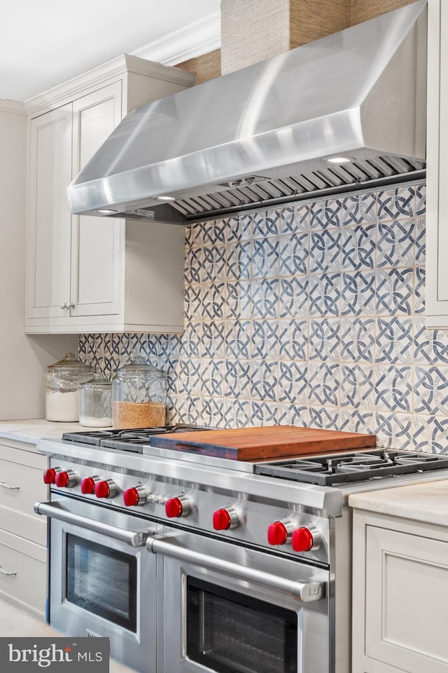 kitchen with tasteful backsplash, white cabinetry, wall chimney exhaust hood, and range with two ovens