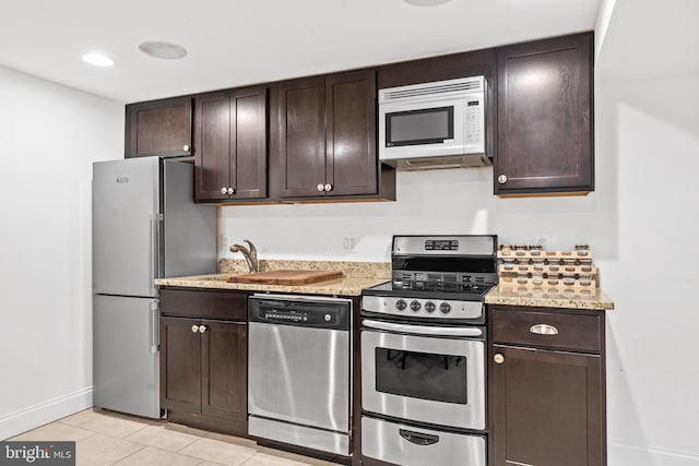 kitchen with dark brown cabinetry, light stone countertops, light tile patterned flooring, and appliances with stainless steel finishes