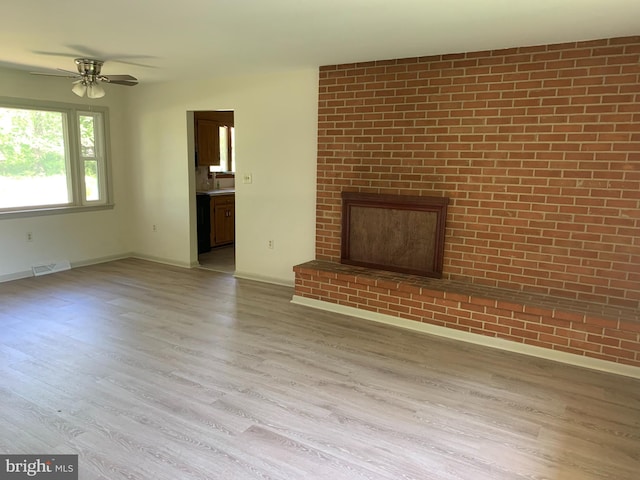 unfurnished living room with ceiling fan, brick wall, a brick fireplace, and hardwood / wood-style floors