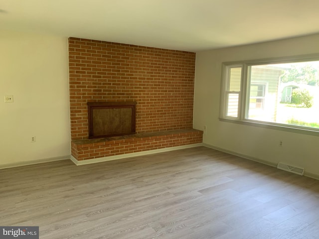 unfurnished living room with a wealth of natural light, brick wall, a brick fireplace, and hardwood / wood-style floors