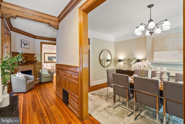 dining room featuring beam ceiling, wood-type flooring, ornamental molding, and a chandelier