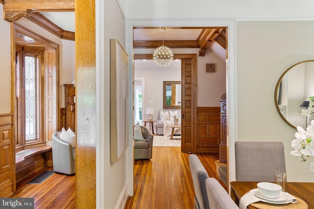 hallway with hardwood / wood-style floors, beam ceiling, crown molding, and an inviting chandelier