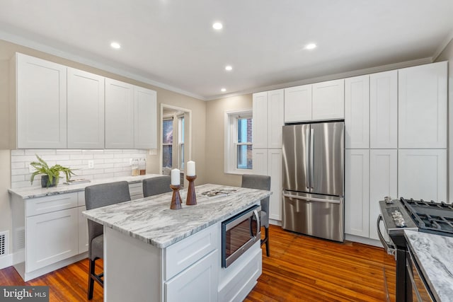 kitchen featuring a breakfast bar, dark wood-type flooring, white cabinets, light stone counters, and stainless steel appliances