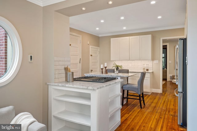 kitchen featuring light stone countertops, a kitchen bar, decorative backsplash, white cabinets, and appliances with stainless steel finishes