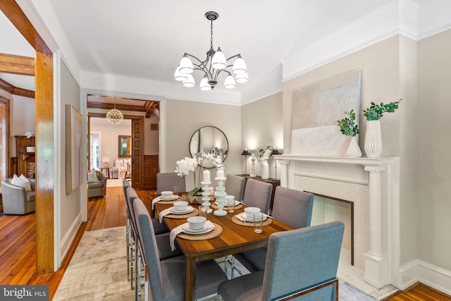 dining room featuring beam ceiling, a tile fireplace, light hardwood / wood-style flooring, crown molding, and a chandelier