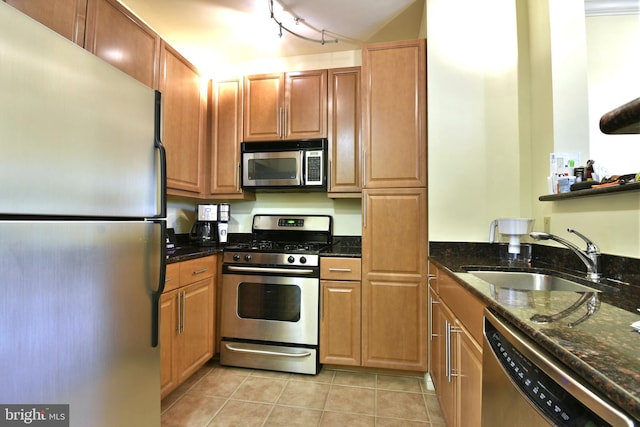 kitchen with light tile floors, stainless steel appliances, dark stone countertops, rail lighting, and sink