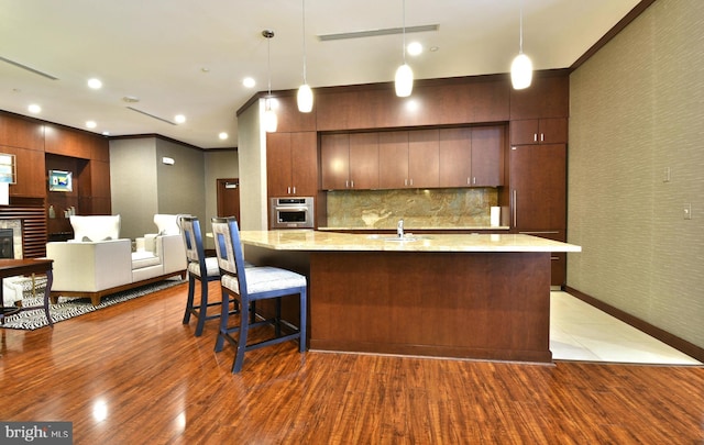 kitchen featuring hardwood / wood-style floors, tasteful backsplash, stainless steel oven, a center island with sink, and pendant lighting