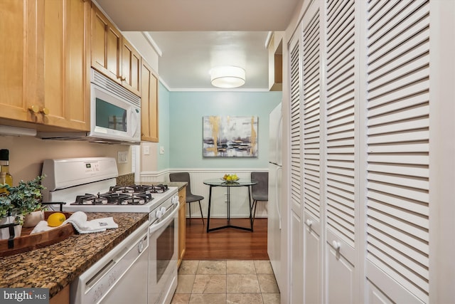 kitchen featuring light brown cabinetry, dark stone countertops, ornamental molding, and white appliances