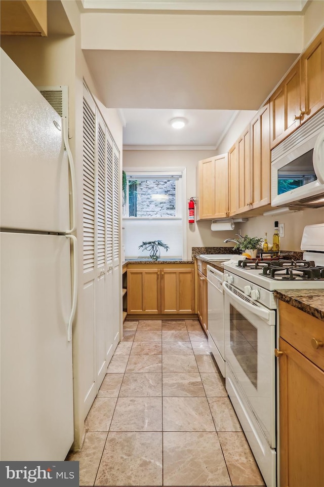 kitchen with dark stone counters, light tile patterned flooring, white appliances, light brown cabinets, and ornamental molding