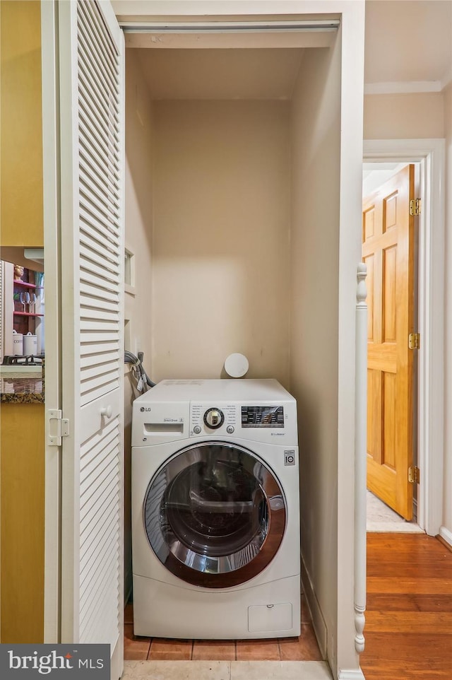 washroom with light wood-type flooring, ornamental molding, and washer / dryer