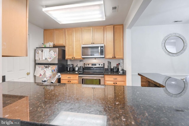 kitchen with dark stone counters, light brown cabinets, stainless steel appliances, and sink