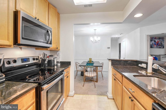 kitchen featuring sink, dark stone countertops, a chandelier, light tile patterned floors, and appliances with stainless steel finishes