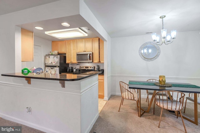 kitchen with kitchen peninsula, appliances with stainless steel finishes, light brown cabinets, decorative light fixtures, and a notable chandelier