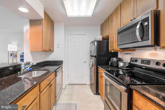 kitchen with dark stone countertops, sink, light tile patterned floors, and stainless steel appliances